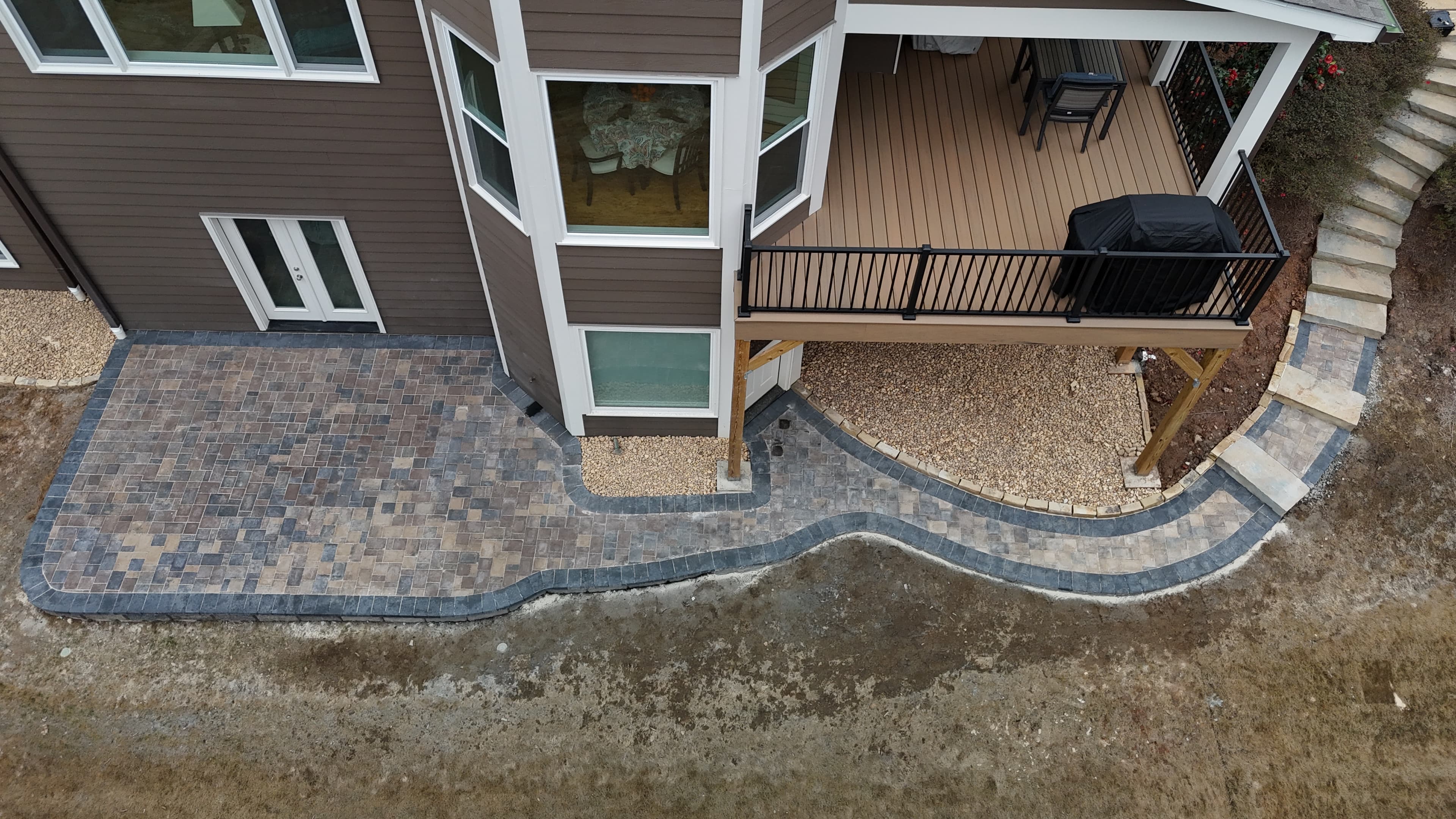 Aerial view of a multi-toned paver patio and curved walkway behind a brown house.