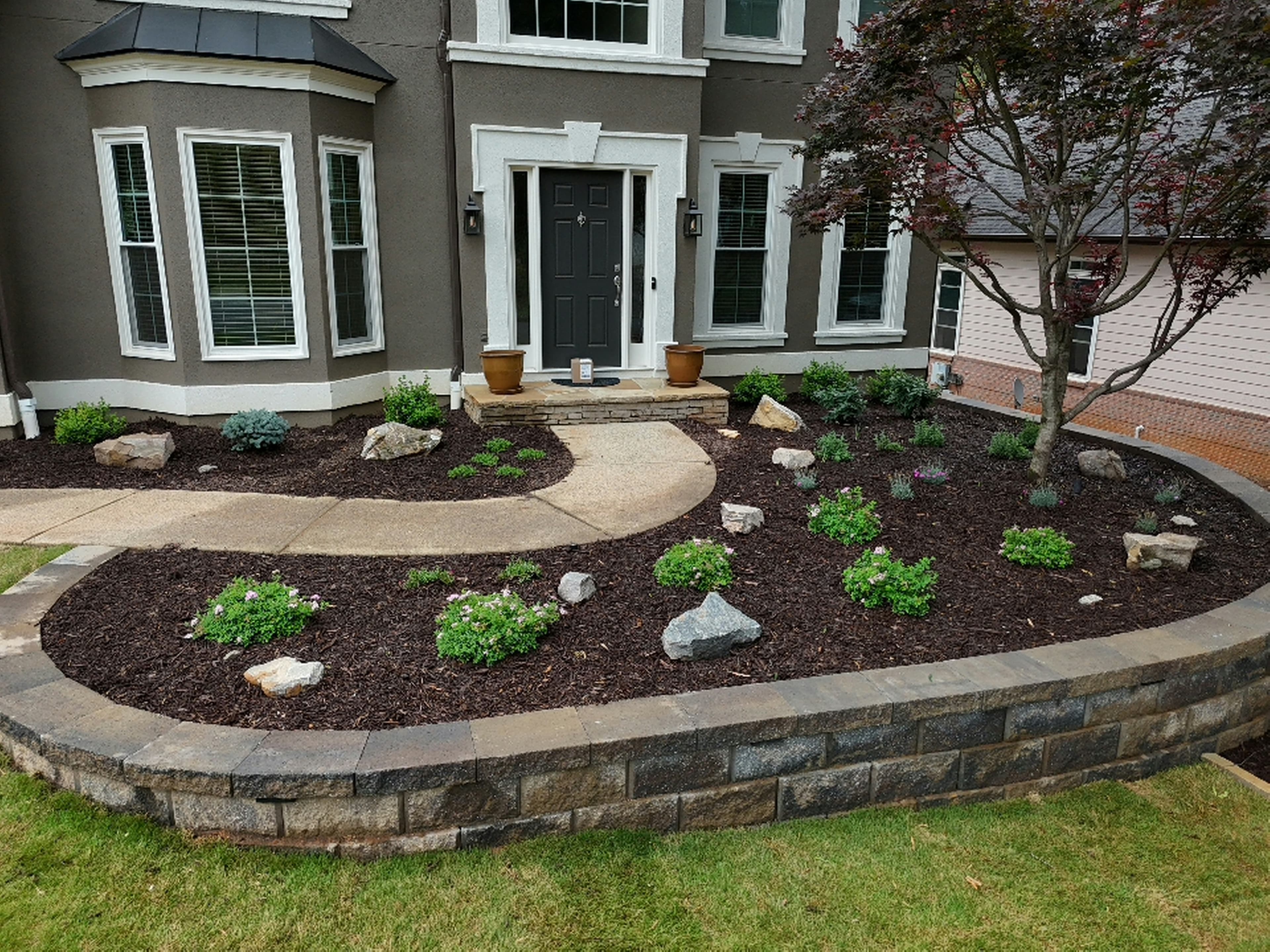 Landscaped garden with a stone retaining wall and curved walkway in front of a house.