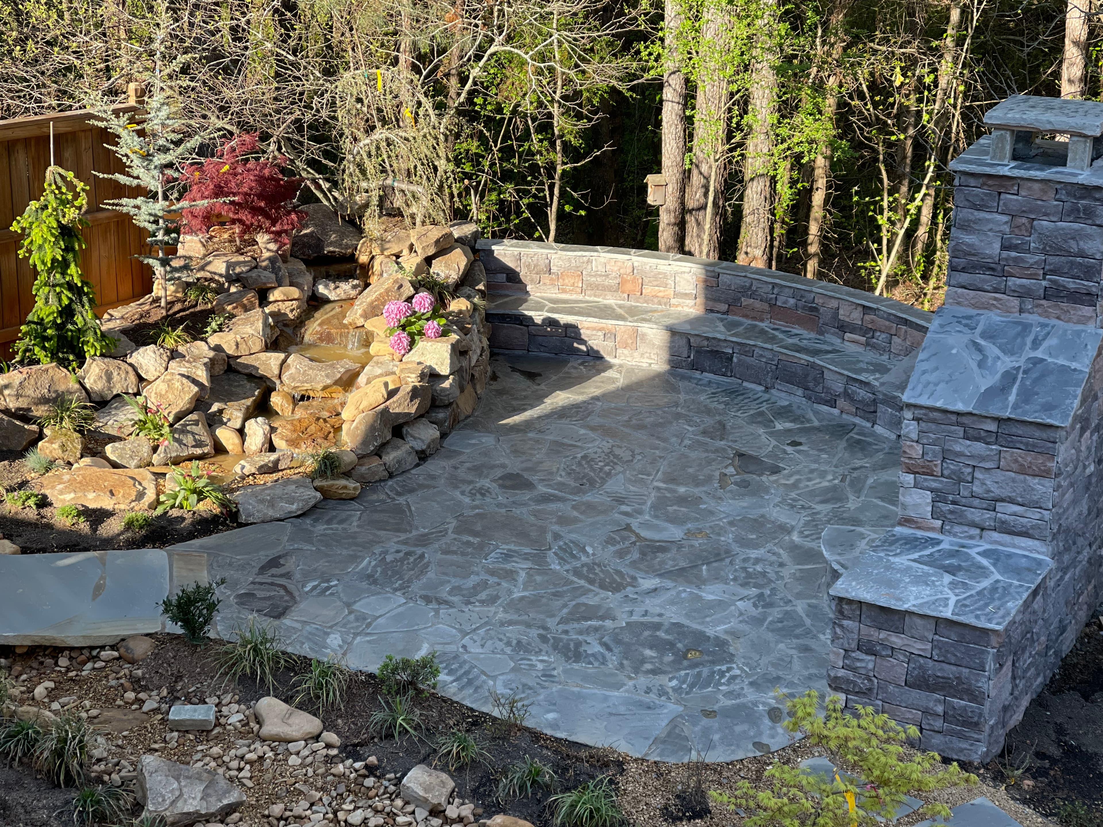 Flagstone patio with a rock waterfall, curved stone bench, and a large outdoor fireplace.