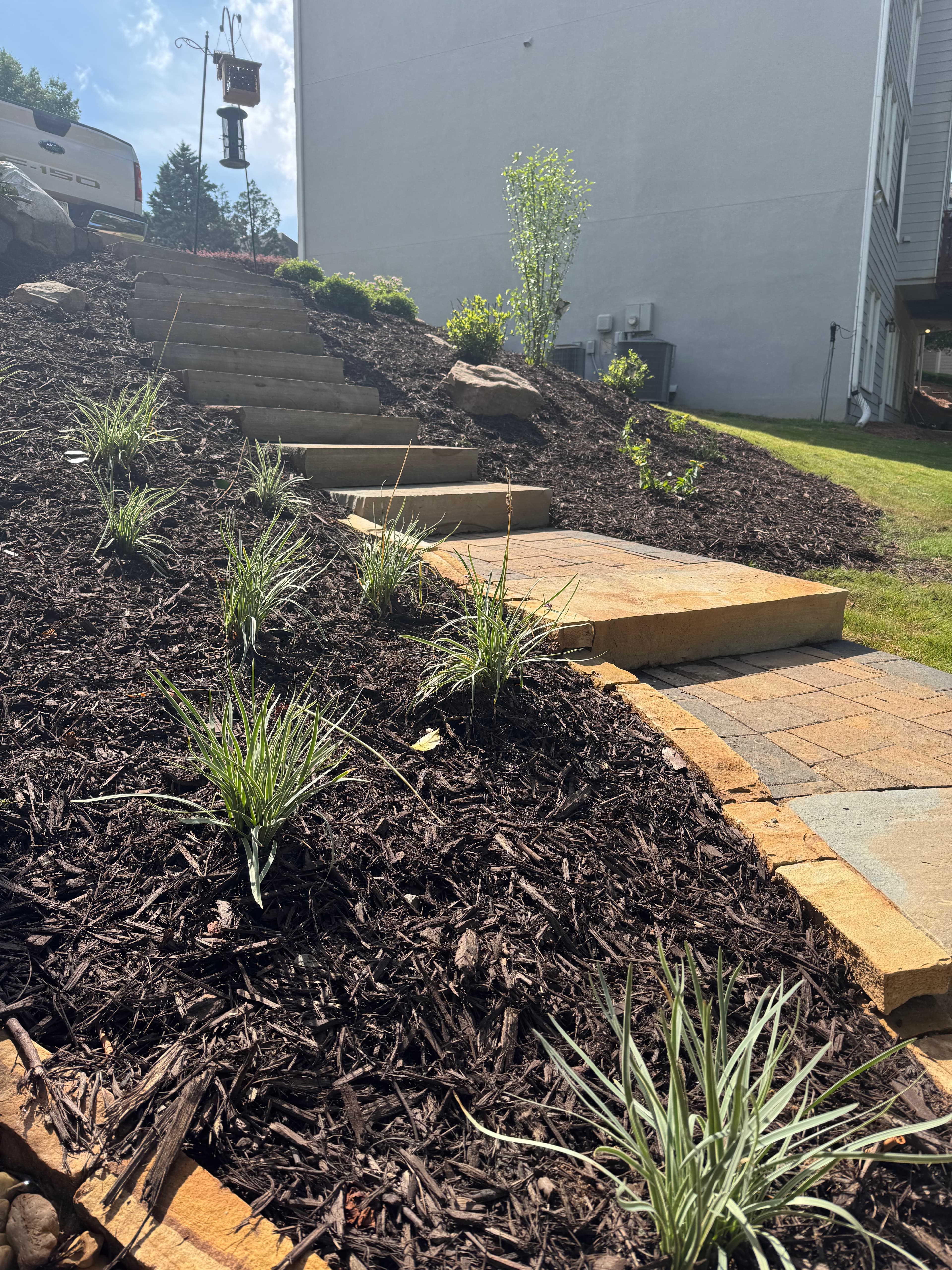 Stone steps lead up a landscaped slope with dark mulch and small ornamental grasses.