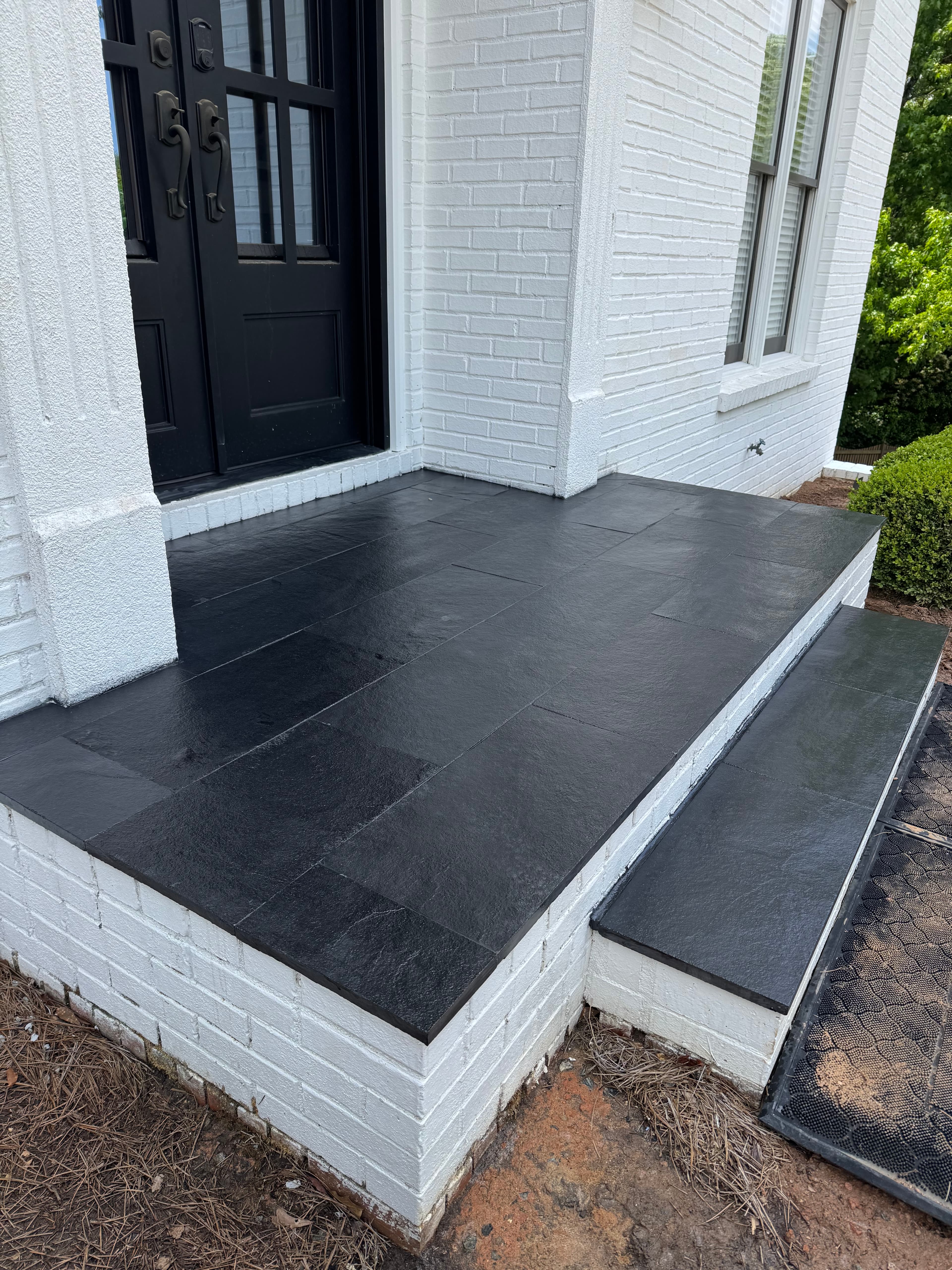 Black front door and dark slate tile steps on a white painted brick house.