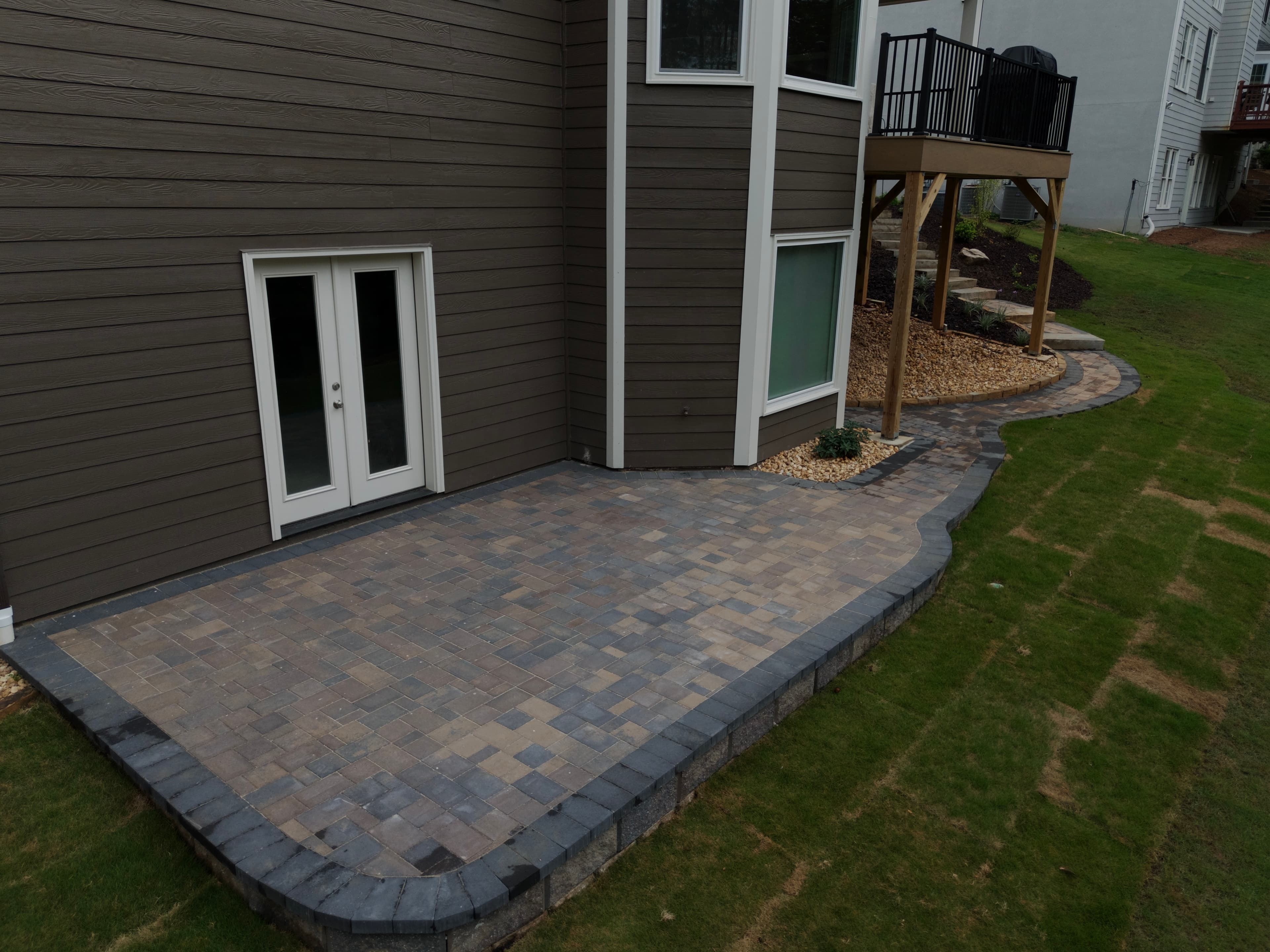 Stone paver patio and curved walkway installed behind a brown house with white French doors.